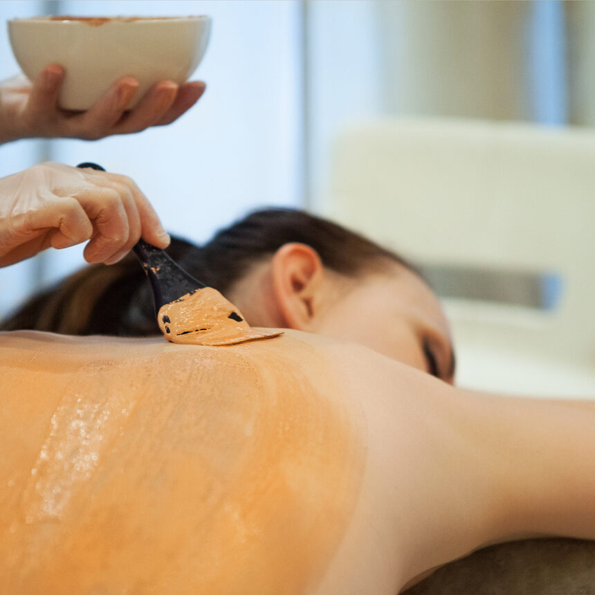 Beautiful relaxed woman having clay body mask apply by beautician in the spa salon